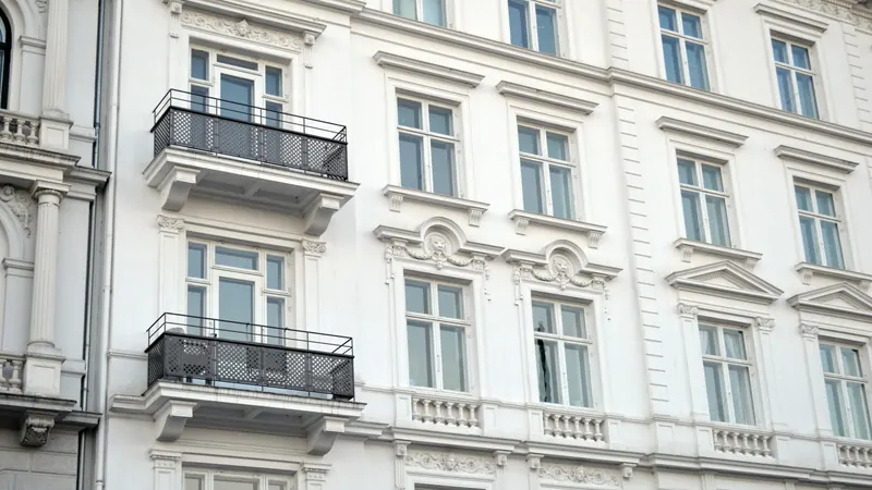 Weiße Altbaufassade mit Stuck, hohen Sprossenfenstern und schmiedeeisernen Balkonen