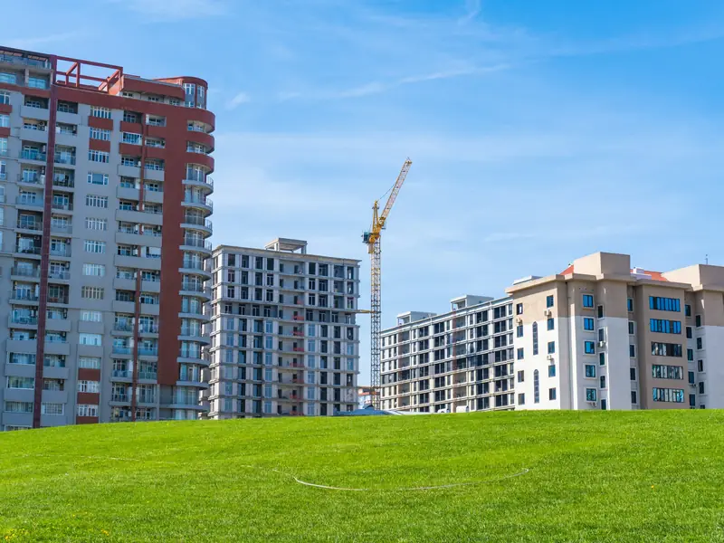 Neue Wohnhochhäuser im Bau mit Baukran vor blauem Himmel, im Vordergrund eine Wiese
