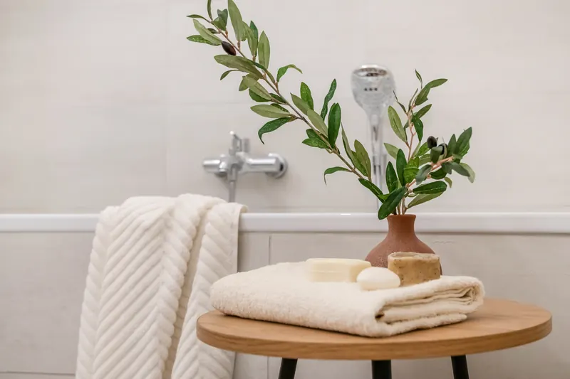 Beistelltisch mit Handtüchern und Olivenzweig neben der Badewanne