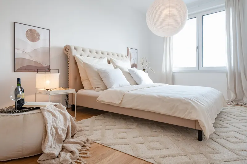 Schlafzimmer mit Polsterbett am Fenster, Hocker und Wandbild
