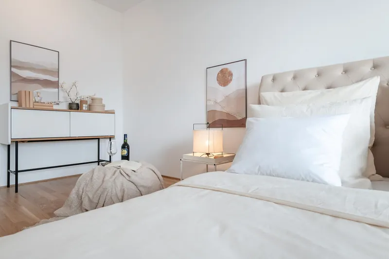 Schlafzimmer mit Polsterbett, weißer Bettwäsche, Nachttischleuchte und Sideboard