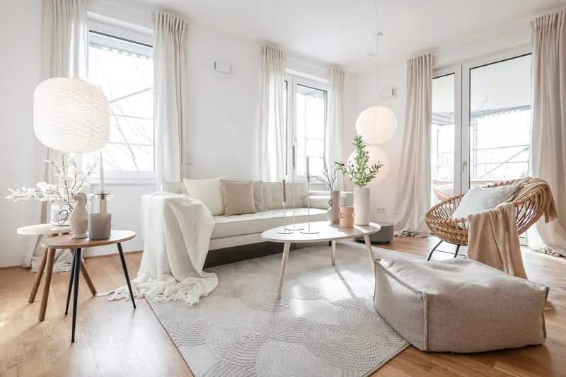 Helles Wohnzimmer mit beigem Sofa, Rattansessel, Papierleuchten und bodentiefen Fenstern