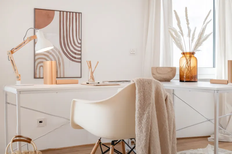 Arbeitsplatz mit weißem Schreibtisch, Schreibtischleuchte und Schalenstuhl am Fenster
