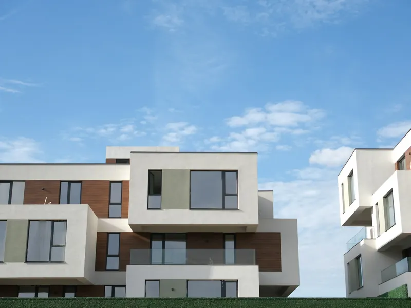 Moderne, helle Mehrfamilienhäuser mit klaren Kubaturen unter blauem Himmel mit leichten Wolken
