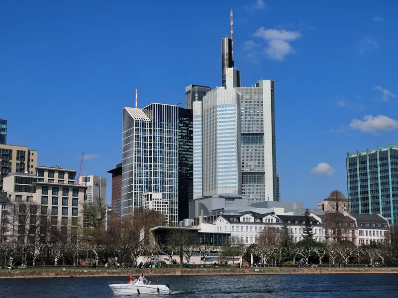 Frankfurter Bankenviertel mit Hochhäusern am Mainufer unter blauem Himmel, im Vordergrund ein Boot auf dem Main